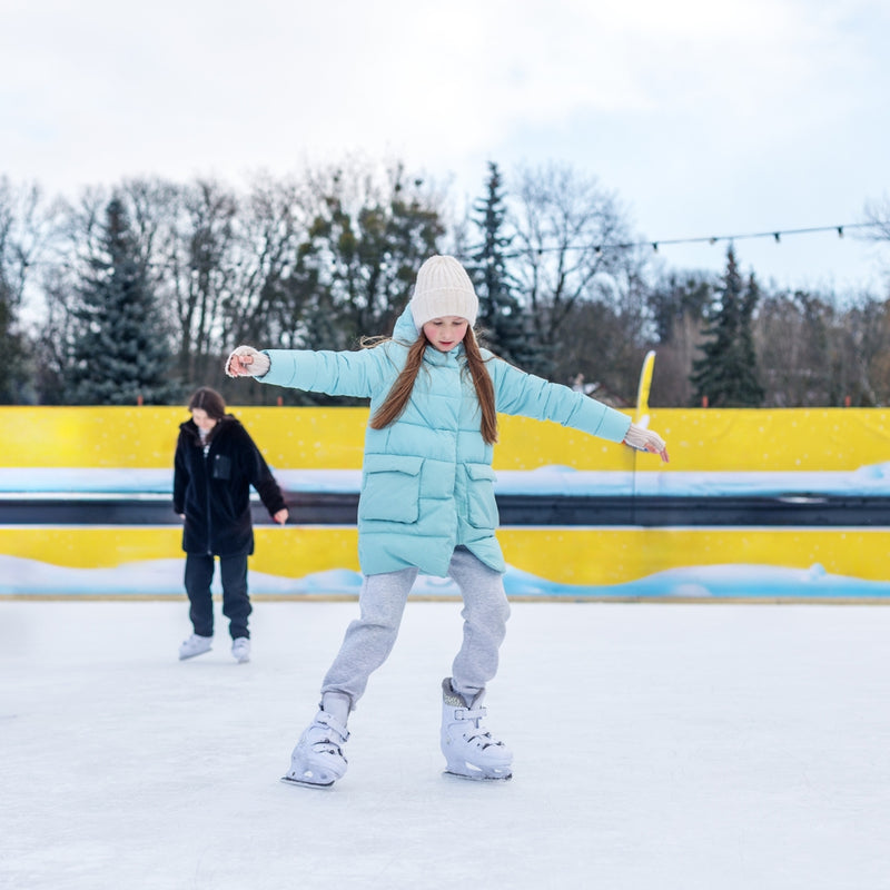 Person ice skating on a frozen lake with a yellow fence and trees in the background