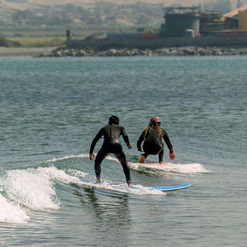 Two people surfing on a body of water with a cityscape in the background
